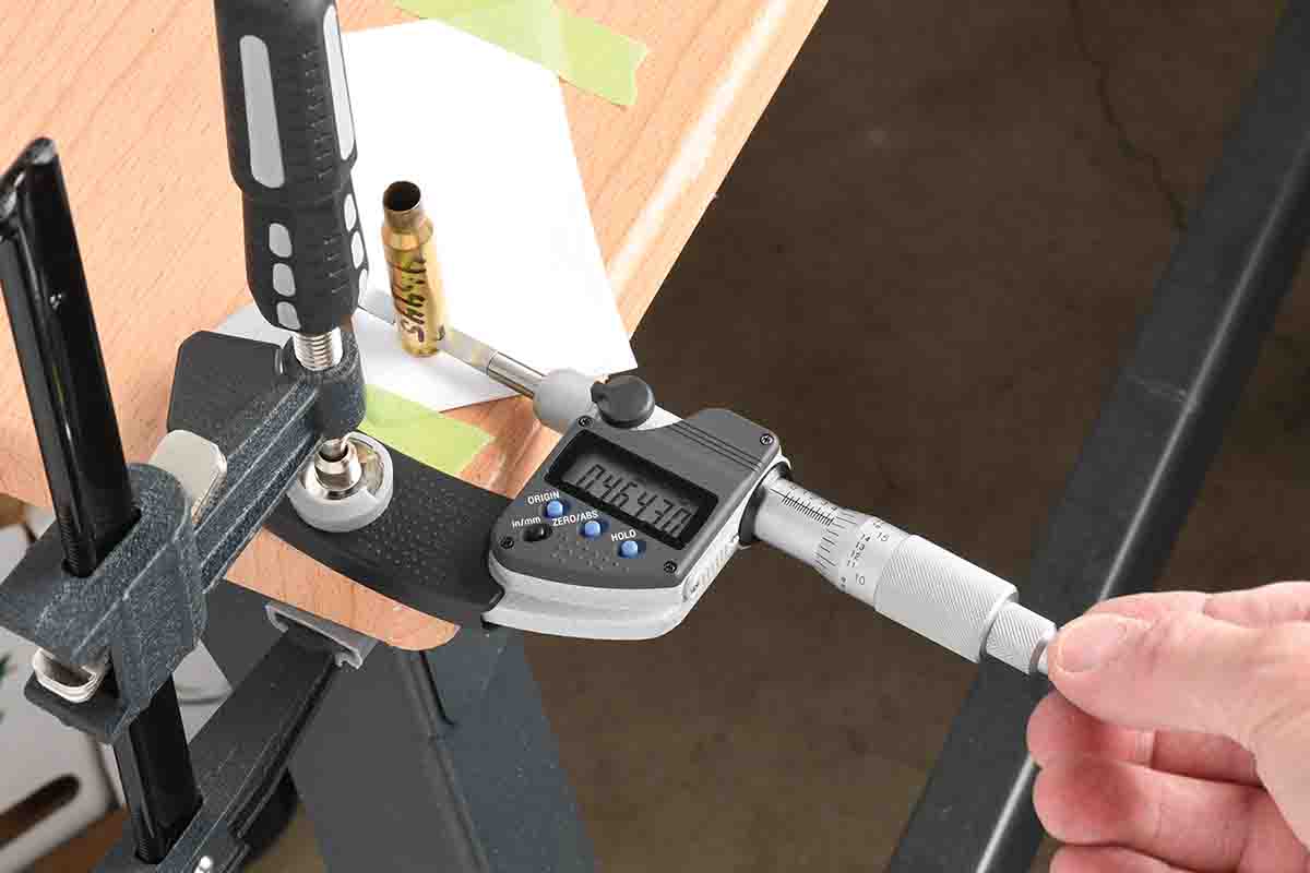 This relatively simple setup can be used to measure case webs. It prevents hand-holding the case or the micrometer. By shimming up the tabletop surface, the case is presented to the blade jaws at the proper height relative to the extractor groove and expansion ring, and with the micrometer jaws square with the brass surface.